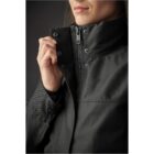 Person zipping up a dark jacket with a high collar.