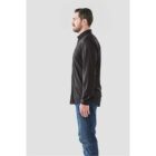 Side view of a person in a black shirt and blue jeans standing against a plain background.