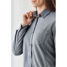 Person wearing a gray button-up shirt with a chest pocket, adjusting the collar.