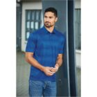 Man in a blue polo shirt and jeans leaning against a metal beam outdoors.