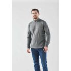 Man in gray zippered sweater and blue jeans stands against a plain white background.