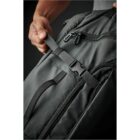 Hand adjusting strap on a sleek, dark gray backpack with multiple zippers.