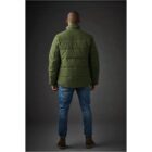 Man in green puffer jacket and jeans standing with back to camera against dark background.