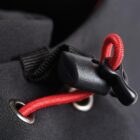 Close-up of a black toggle and red cord on a piece of fabric with metal eyelets.