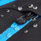 Close-up of a black waterproof zipper with water droplets on blue fabric underneath.
