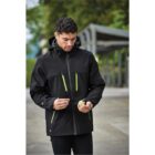 Man in black jacket with green zippers outdoors on a gray path.