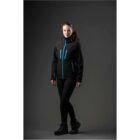 Woman in black and blue outdoor jacket and boots poses confidently against a dark background.