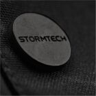 Close-up of a round metal button with STORMTECH embossed on a textured fabric surface.