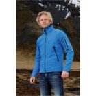 Person in blue jacket and jeans standing in front of mountainous landscape.
