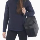 Person holding a large black shoulder bag against a plain background.