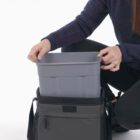 Person placing a gray container into a black insulated bag.