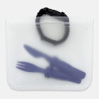 A frosted, reusable silicone bag contains a dark-colored spork, knife, and a rolled-up wristband or strap on top. The bag is sealed and set against a plain background.