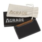 A black cardholder with white stitching is displayed next to a sand-colored drawstring pouch bearing the text GRADE. They are placed on top of a black box with a similar GRADE logo and the tagline BECAUSE EVERYONE DESERVES AN UPGRADE.