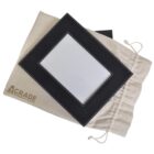 Black rectangular photo frame with white stitching, placed on a beige drawstring pouch. The pouch has AGRADE printed on it in brown letters. The frames photo area is blank, and the pouch appears to be made of a soft, natural fabric.