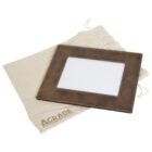 Brown leather photo frame with a rectangular opening, resting on a beige drawstring bag labeled A GRADE. The background is white.