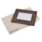 A brown leather photo frame with a glass front, placed on a beige cloth bag labeled AGRADE. The frame has a rectangular opening for a photo.