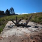 A multi-tool with various open metal tools lies on a wooden surface outdoors. The background features a grassy field and a partially visible building under a clear blue sky.
