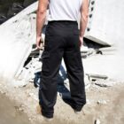 A person in a white t-shirt and black cargo pants stands with their back to the camera, facing a pile of broken concrete debris. The scene suggests a construction or demolition site.