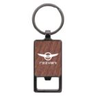 A keychain featuring a wooden rectangular section with the Rezvani logo and name in white. The top has a metal ring for attaching keys, and the bottom has a metal bottle opener.