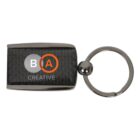 Rectangular keychain with a black carbon fiber pattern and a metal frame. Features a B in a gray circle, an A in an orange circle, and the word CREATIVE below in white text. Attached to a circular metal ring.