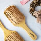 Two LOréal wooden hairbrushes with light bristles are on a light surface. Nearby, theres a leopard-print scrunchie, a beige ruffled scrunchie, and a pink beauty product tube.