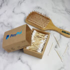 An open box of wooden cotton swabs with a brown PayPal label is on a marble surface. Nearby are a few loose swabs and a wooden hairbrush with the brand Gillette printed on the handle.