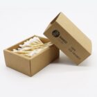 A cardboard box labeled Bamboo range with 100% eco-friendly printed on it is open, revealing cotton swabs with wooden sticks inside. The box and swabs are placed on a white background.