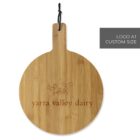 Round wooden cutting board with a handle and a black hanging loop. Engraved with an outline of a cow and the text yarra valley dairy. Custom logo area indicated in the top right corner.