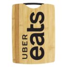 A wooden cutting board with the Uber Eats logo printed on it in bold black letters. The board has a black handle at the top.