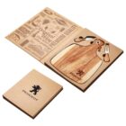 A brown Peugeot-branded gift set includes a wooden cutting board and two cheese knives with wooden handles. The set is displayed in an open cardboard box with decorative text and a closed box beside it.