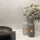 A kitchen counter with a black frying pan on a gray stove. Next to it are two bottles with Hard Rock Cafe logos, one white and one gray, and a bouquet of dried flowers in the background.