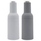 Two cylindrical, modern salt and pepper grinders stand side by side against a white background. The left grinder is light gray, and the right grinder is dark gray. Both have a sleek, matte finish with stainless steel tops.