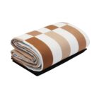 Folded checkered blanket with wide brown, beige, and white stripes, resting on a black surface.