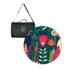 A folded black blanket with a shoulder strap and a green Heineken logo next to a colorful round mat featuring abstract floral designs in red, green, and yellow on a dark background.