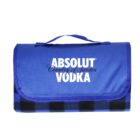 A folded blue picnic blanket with a handle, featuring the Absolut Vodka logo and Country of Sweden text. The blanket has a checkered pattern in darker blue tones.