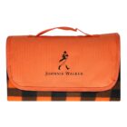 An orange picnic blanket with a handle, folded neatly. The front displays the silhouette of a striding man and the text Johnnie Walker. The bottom edge has a black and orange checkered pattern.
