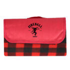 Red and black plaid picnic blanket folded with a red flap. The flap features the Fireball Whisky logo, depicting a dragon. A handle is attached to the flap for easy carrying.