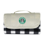 Folded picnic blanket with a beige flap and handle featuring the Starbucks logo. The blanket pattern is black and white checkered.