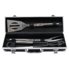 A set of stainless steel grilling tools in a black carrying case with a handle. The tools include a slotted spatula, tongs, and a fork, all secured with elastic straps inside the case.