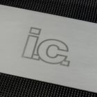 Silver metal square on textured black background, featuring engraved letters i.c. in a bold, modern font.