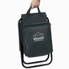 A hand carries a green folding chair with a built-in bag. The bag features a white logo with the text “BRANDS construction” and a simple building skyline design. The chair has a black metal frame and fabric seat.