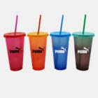 Four colored plastic cups with matching lids and straws stand in a row against a white background. Each cup is branded with a Puma logo and varies in color: pink, orange, blue, and green.