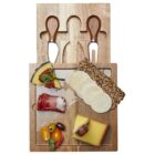 Wooden cheese board with cheeses, sliced meats, and assorted garnishes. Two cheese knives and a fork are nestled in dedicated slots above the board. Various cheese slices, a rolled cured meat, grapes, and cherry tomatoes are arranged on the board.