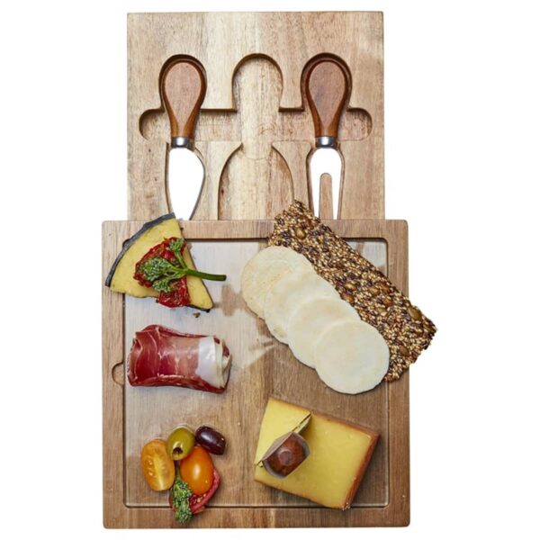 A wooden cheese board with assorted cheeses, meats, and crackers. Two knives and a fork with wooden handles are embedded in the board. Various accompaniments, including grapes and tomatoes, are also on the board.