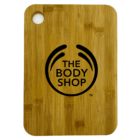 A wooden cutting board with a rounded corner and a circular hole near the top. It features The Body Shop logo and text in black in the center.