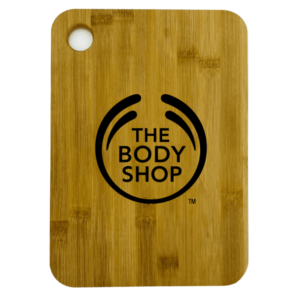 A wooden cutting board with a rounded corner and a circular hole near the top. It features The Body Shop logo and text in black in the center.