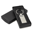A sleek silver metal keychain with a rectangular tag is presented in a black gift box. The keychain is displayed prominently in the box, which is partially open, showcasing its shiny finish.