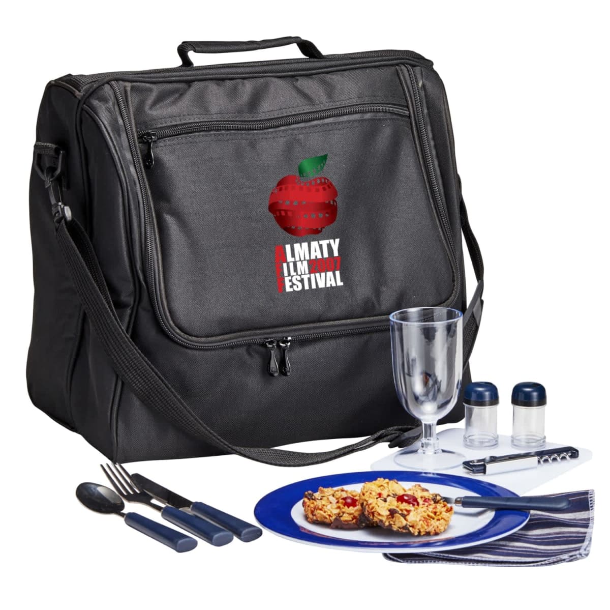 A black insulated picnic bag with Almaty Apple Festival and a red apple logo. In front, a blue plate with food, black-handled cutlery, a clear glass, salt and pepper shakers, a corkscrew, and a folded napkin.