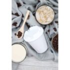 Overhead view of a scene with a takeaway coffee cup, an iced coffee, a milky coffee, and a wooden spoon with coffee beans. Coffee beans are scattered on a gray fabric background.