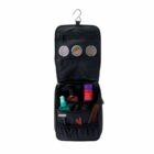 A black hanging toiletry bag with one open flap. Inside are grooming items like a red canister, scissors, a comb, and a deodorant stick. The flap has three mesh pockets containing small round containers. A hook is at the top for hanging.